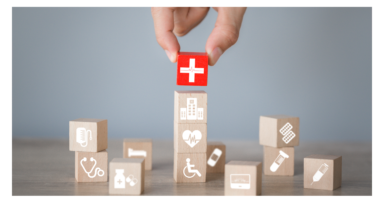 Hand stacking blocks with symbols where the last one placed is all red with a hospital symbol