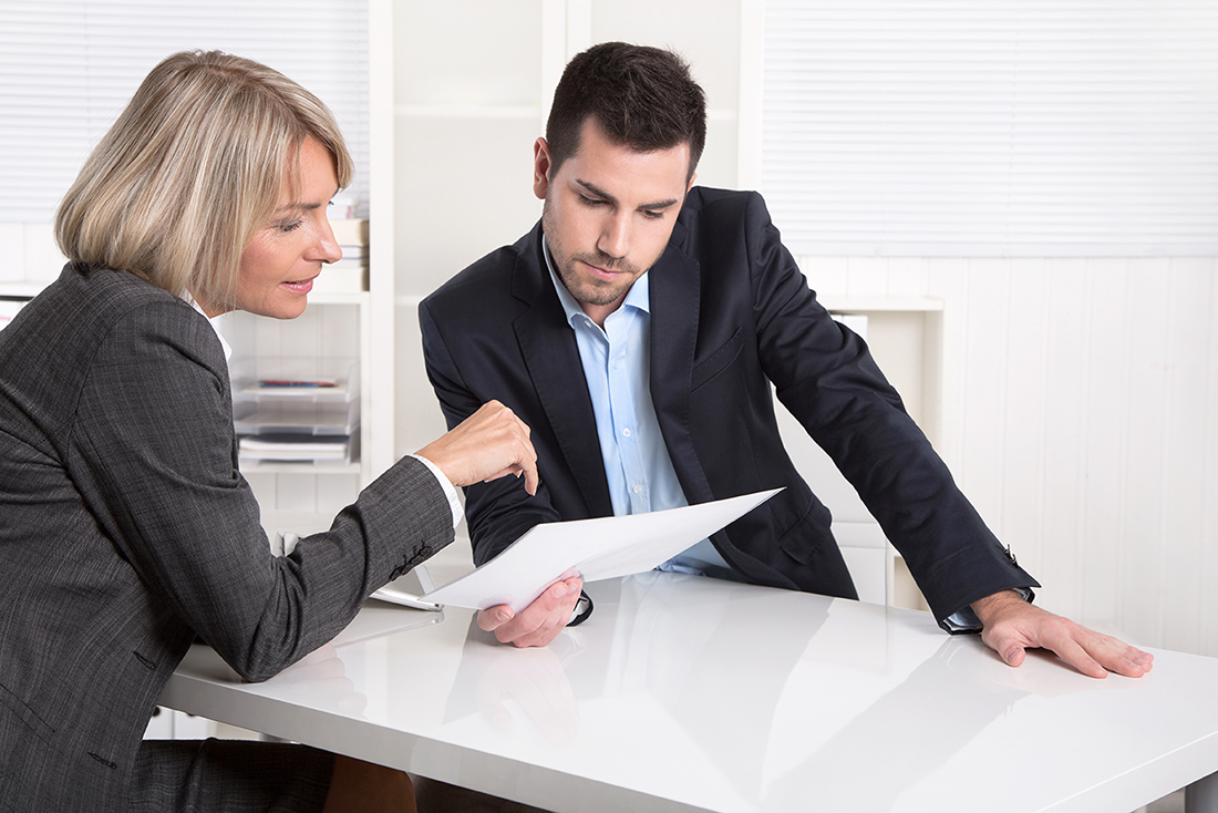 A man and woman in business suits sit at a table reviewing a document
